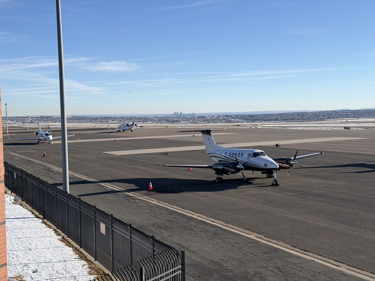 Elevated view of the KBJC airport ramp showing a King Air and business jets with the Denver skyline in the distance