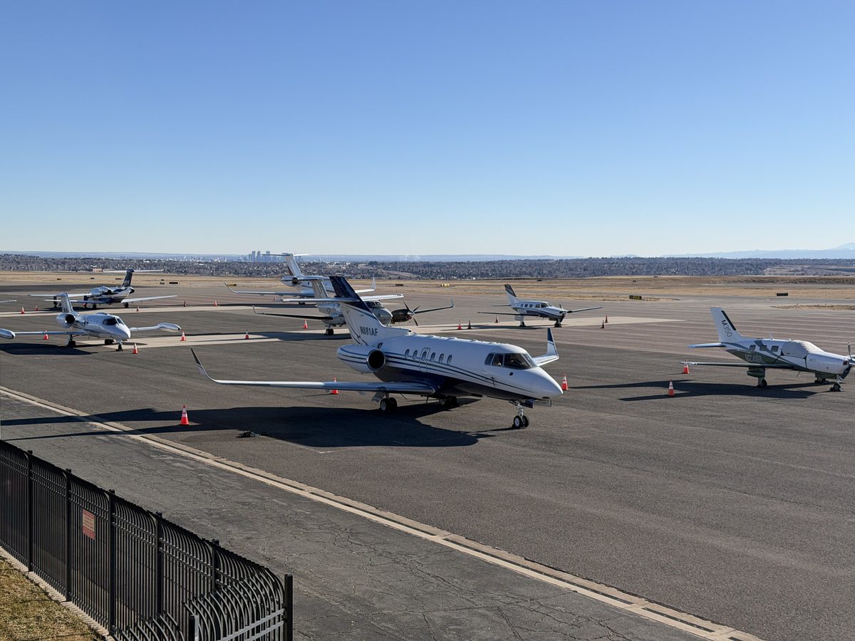 General aviation ramp at Rocky Mountain Metropolitan Airport showing multiple parked aircraft with the Denver skyline on the horizon